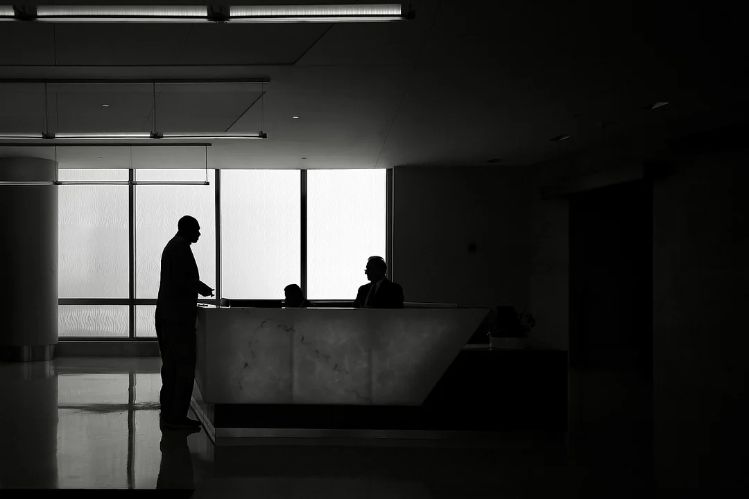 Office lobby in silhouette, a man standing at a pale reception desk against a bright window wall
