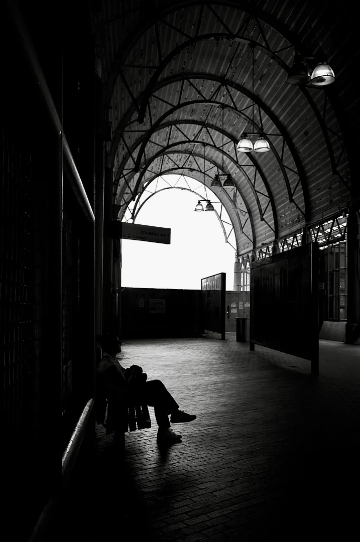 Person sitting alone under the arched iron roof of a covered market walkway