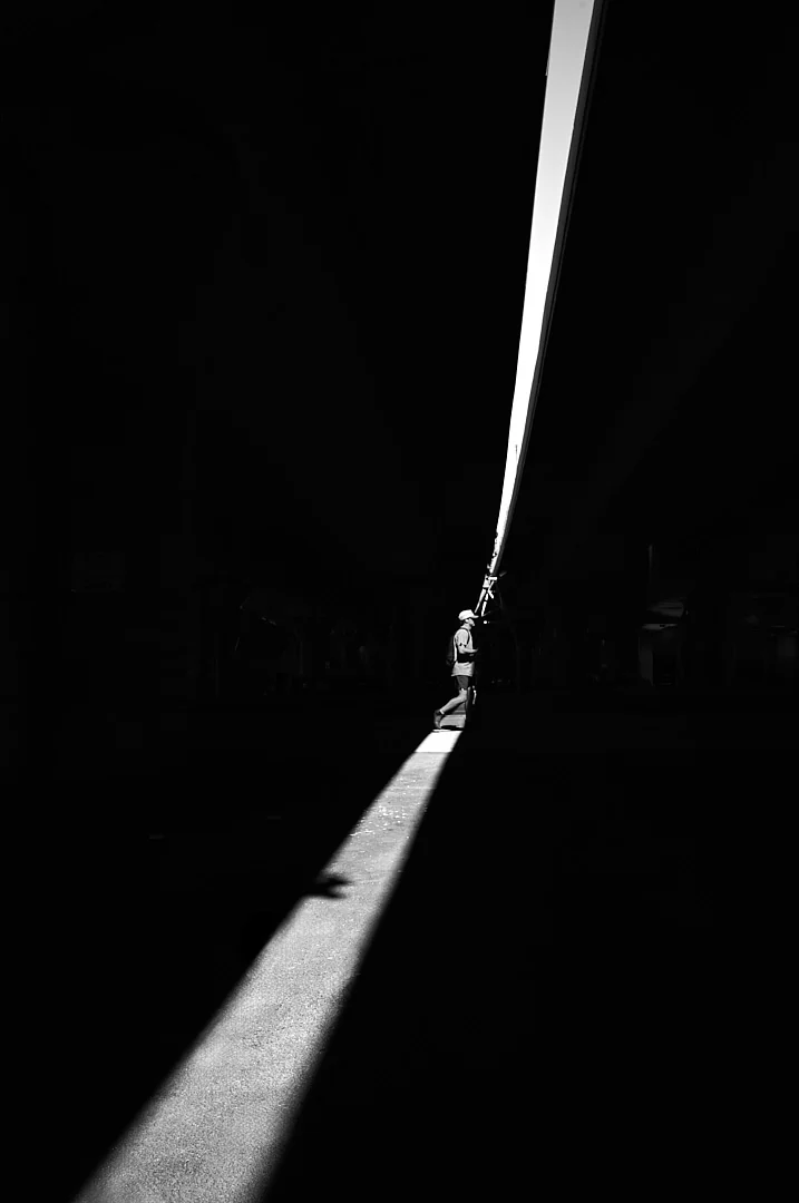 Distant figure walking along a thin diagonal line of light in near darkness