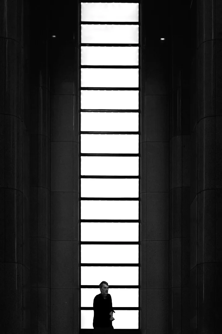 Person standing in a tall window of light framed by dark stone columns