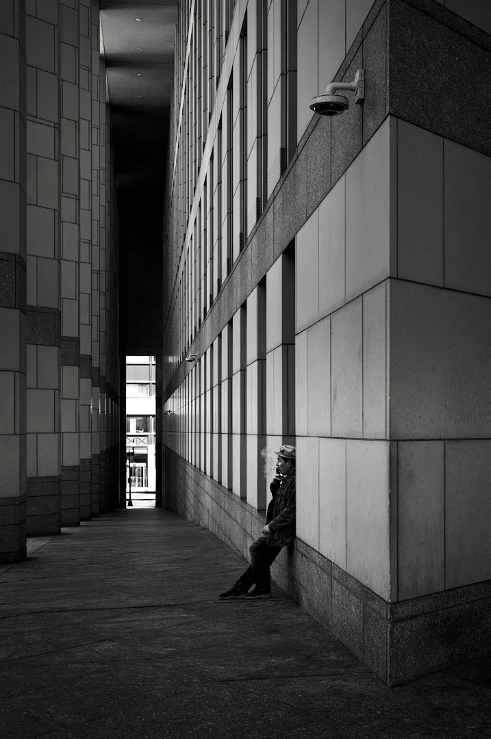 Person sitting against a stone corner in a narrow passage between tall buildings