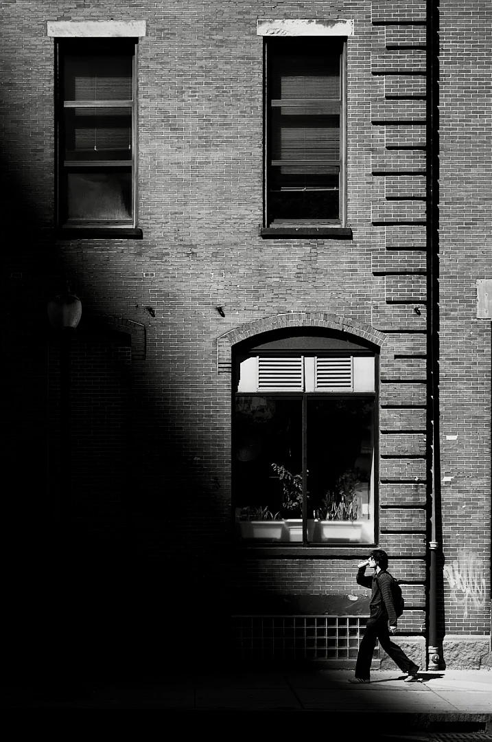 Man walking past a brick building with arched windows and a shop window full of plants