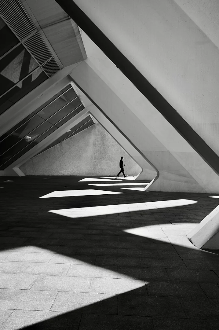 Figure walking through a concrete structure, bright geometric shapes of light on the floor