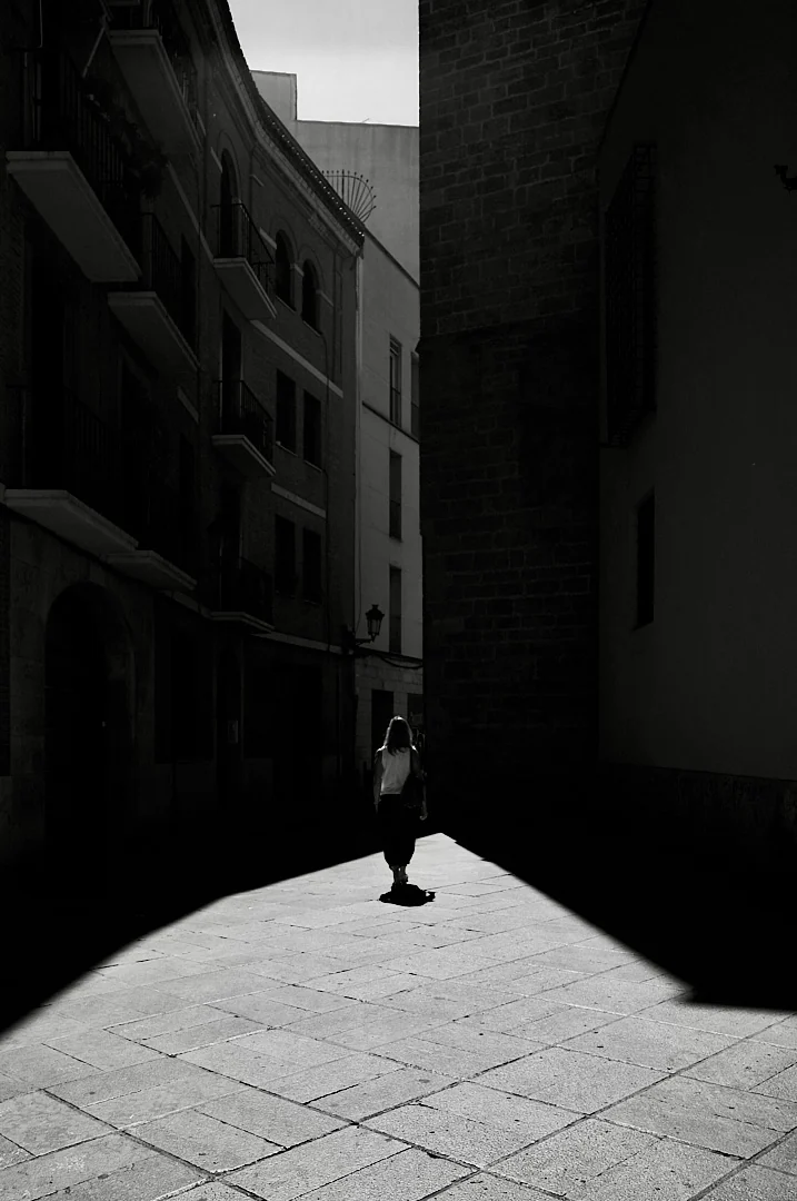 Woman walking into sunlight at the end of a narrow old street