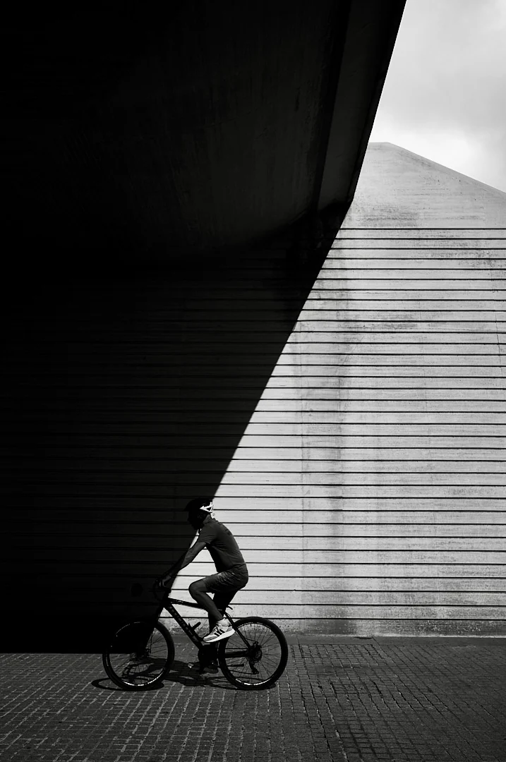Cyclist riding past a ribbed concrete wall divided by a hard diagonal shadow