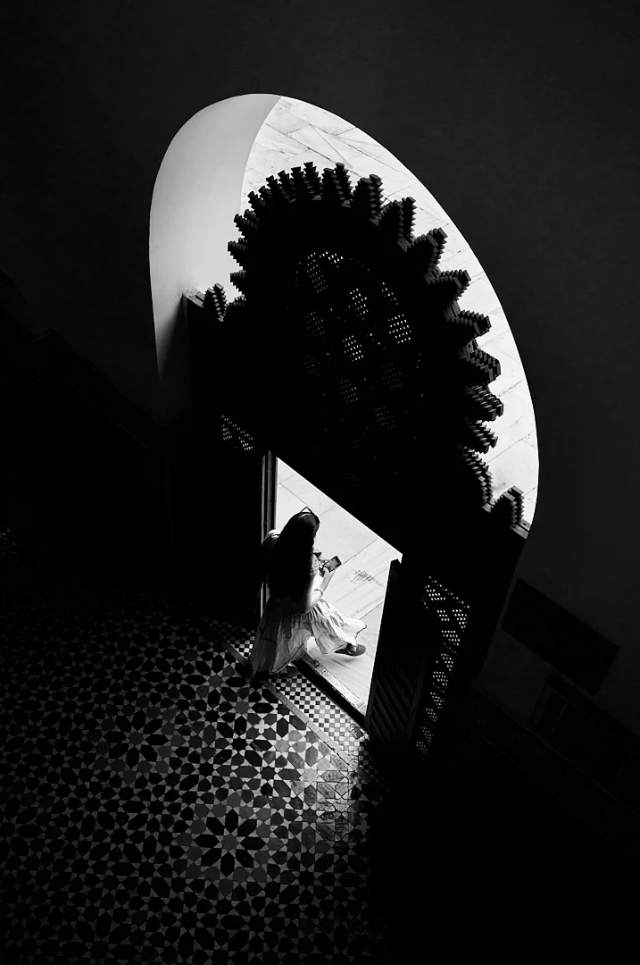 Overhead view of a figure in white stepping through a carved archway onto patterned tiles